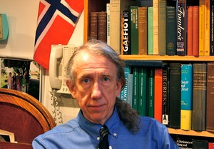 man with ponytail in front of bookshelf