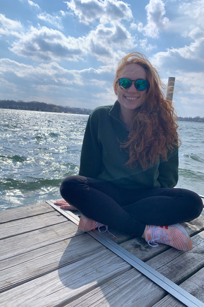 Hannah Kahn in sunglasses sitting on a dock next to the water. 