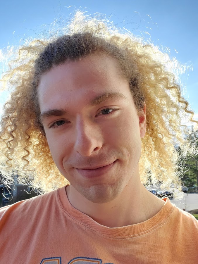a headshot of a man with curly blonde hair wearing a t-shirt
