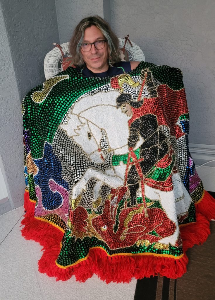 Dr. Christopher Estrada draped in a sequined gola or cape made by maracatu artisan Thony de Lima, depicting Saint George slaying the last dragon.  St.George has a syncretistic association with Yoruba deity Ogun in the Afro-Brazilian religions which play a role in maracatu.  