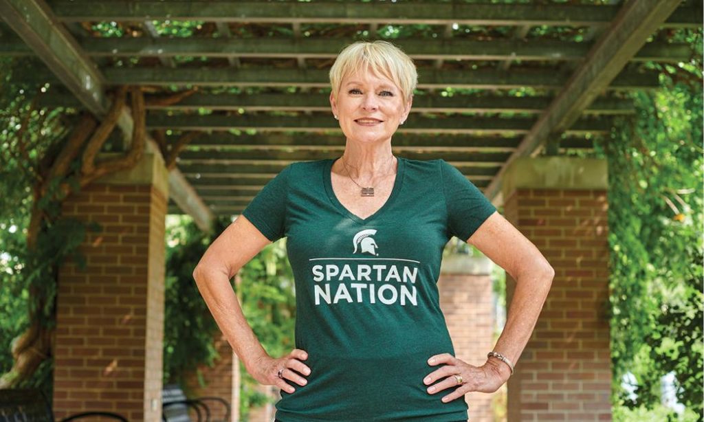 Woman with short blonde hair wearing an MSU tshirt. She is standing with her hands on her hips.