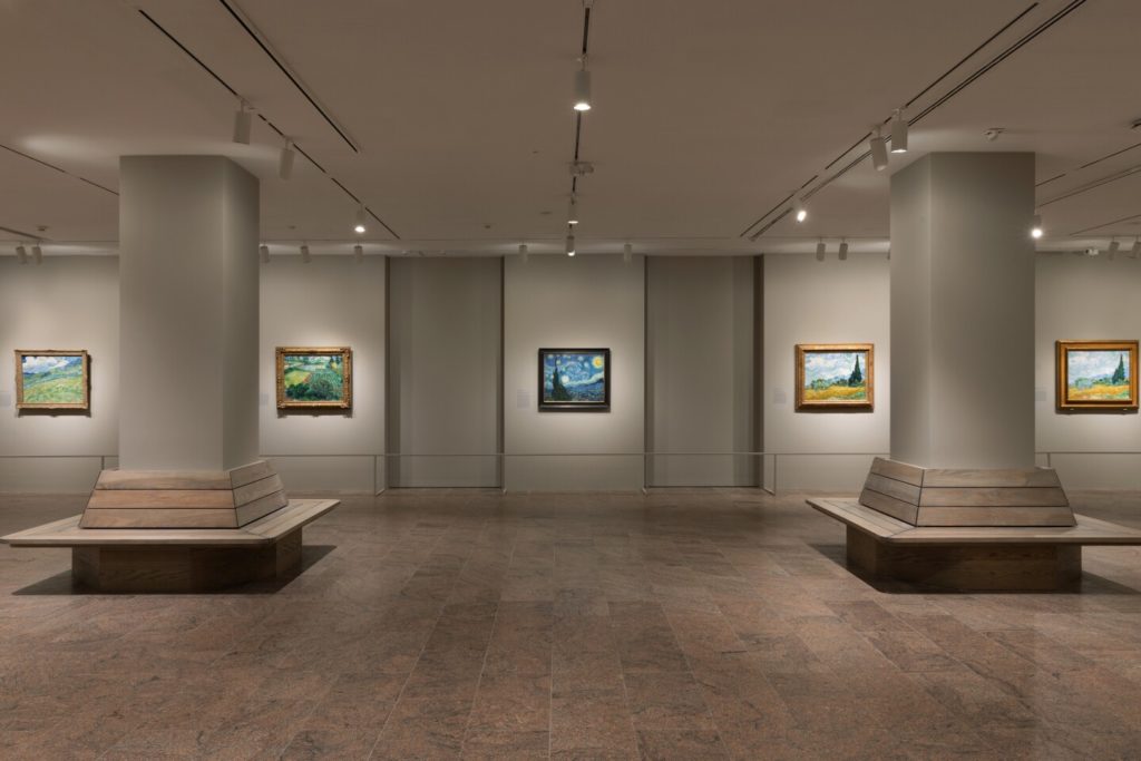 Inside a museum with five Vincent Van Gogh paintings hanging on a wall. 