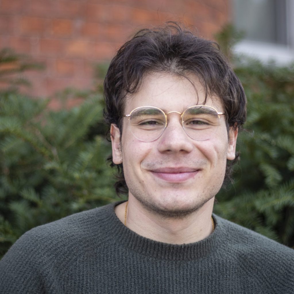 A picture of a man with golden glasses, brown hair, and a green sweater.