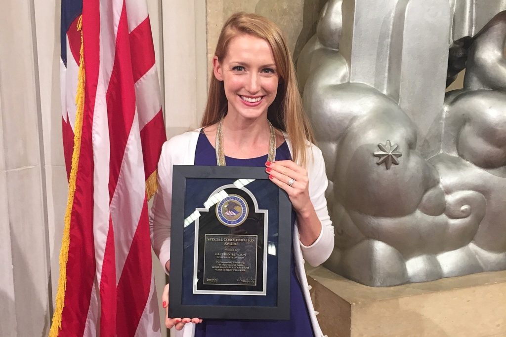 Portrait of Lauyren Haight stands in front of an American flag holding her "Special Commendation Award" from the United States Department of Justice. 