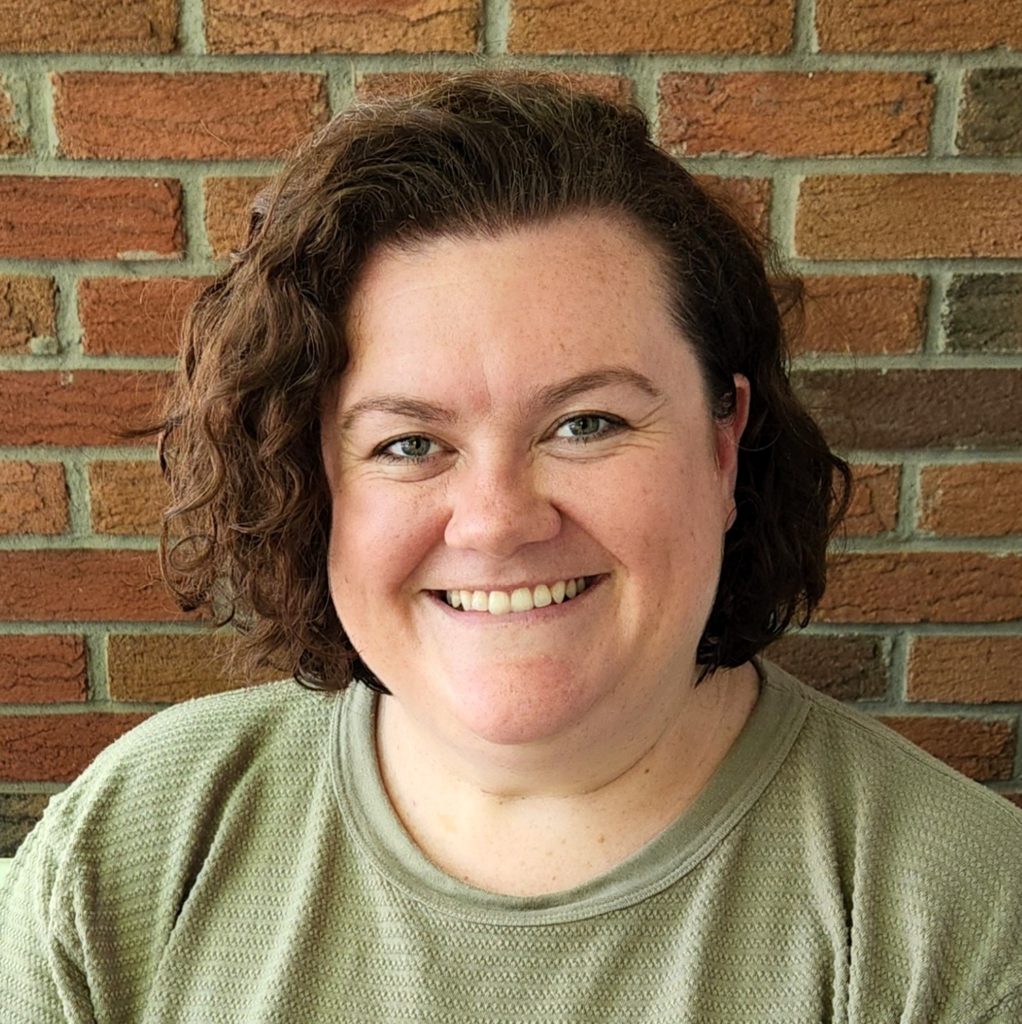 Portrait of a smiling woman with short brown curly hair wearing a green shirt.